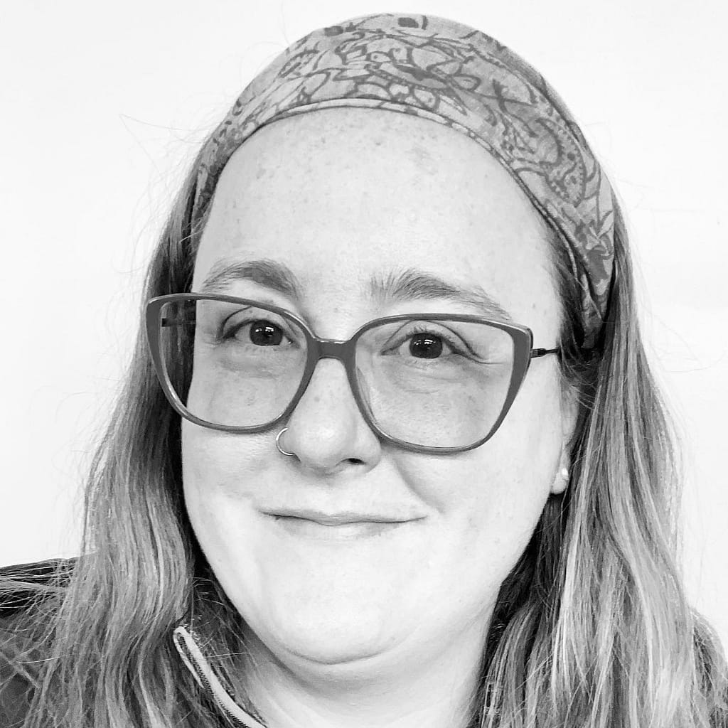 black and white photo of a white 40ish aged woman with glasses wearing a bandana smiling at camera