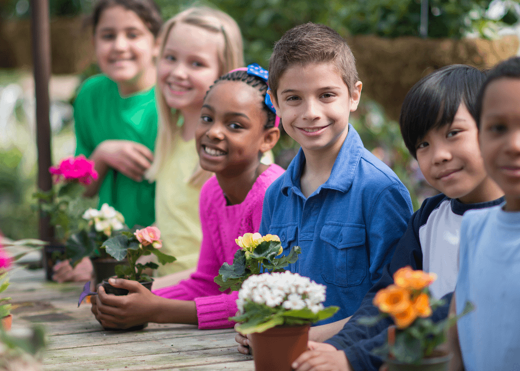 A group of diverse kids standing smiling at the camera and each holding a small potted flower
